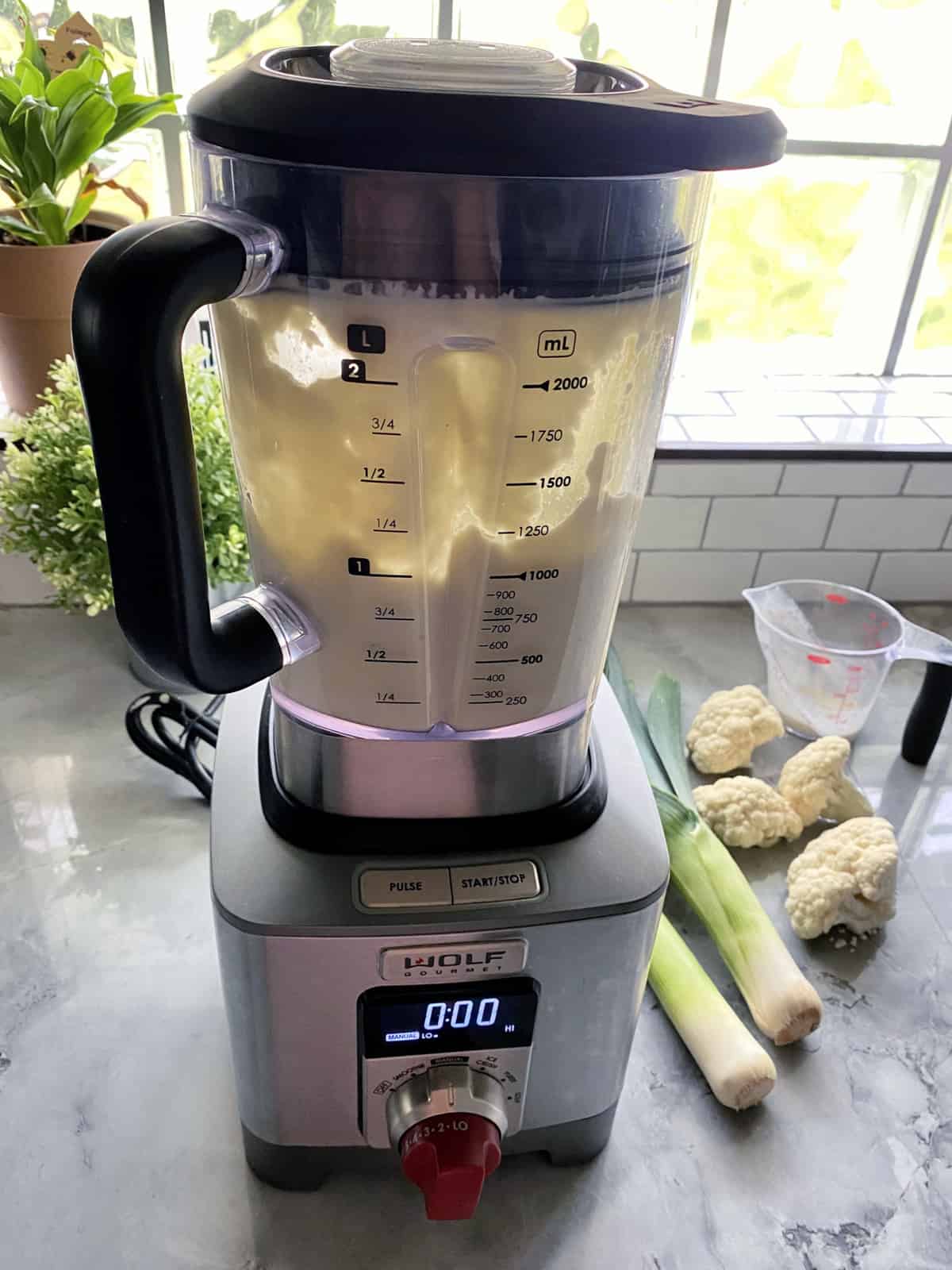 Cauliflower-Leek Puree in the blender on counter next to cauliflower, leeks, and a measuring cup.