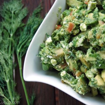 Top view of Avocado & Feta Dip in white bowl with dill blurred in background.