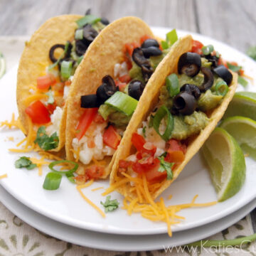 Three plated egg white tacos topped with olives, chives, tomatoes, and cheese garnished with lime and cilantro.