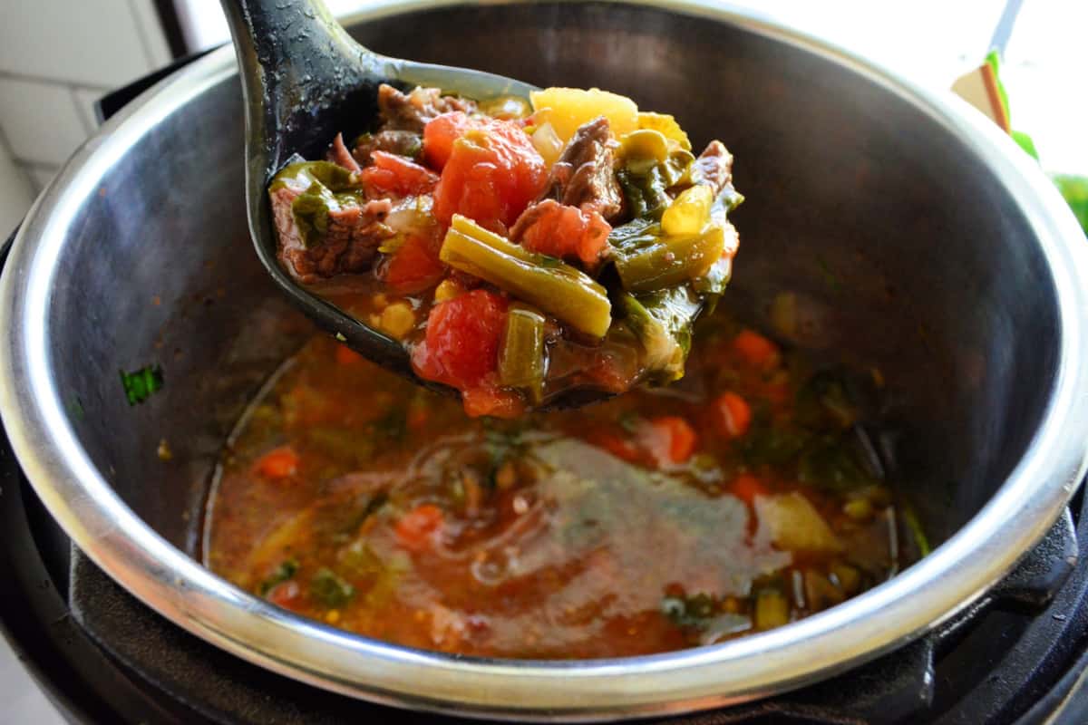 Beef Soup with tomatoes, green beans, corn, and potato being ladled out of the Instant Pot