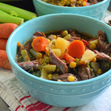 Bowl of Instant Pot Vegetable Beef Soup with fresh carrots and celery in background.