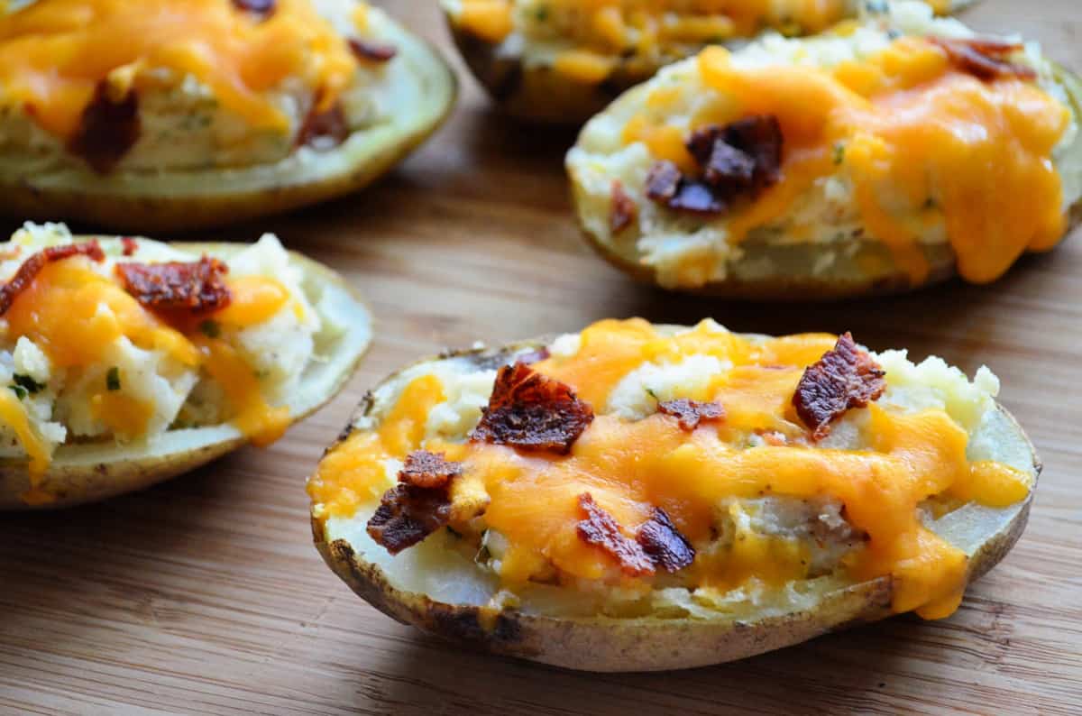 Closeup halved loaded potatoes topped with melted shredded cheddar and crisp bacon bits.