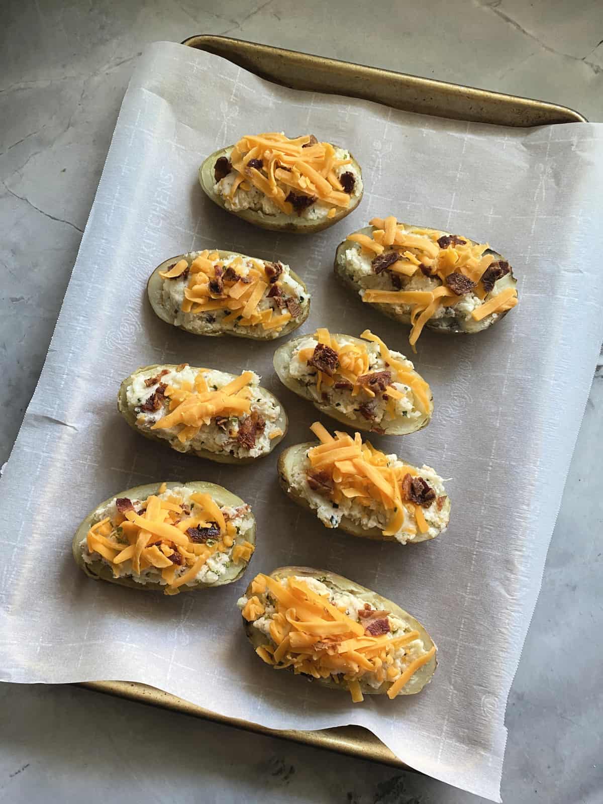 8 halved loaded potatoes topped with shredded cheddar and bacon on wax paper prior to melting.