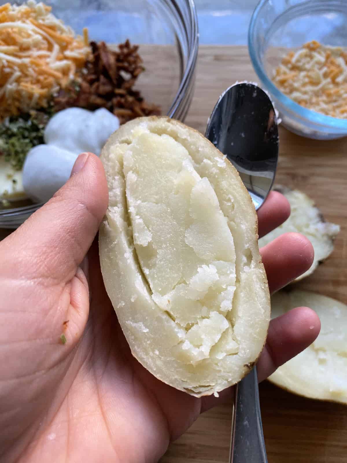 Hand holding potato half close up with spoon, demonstrating how to clean potato out.