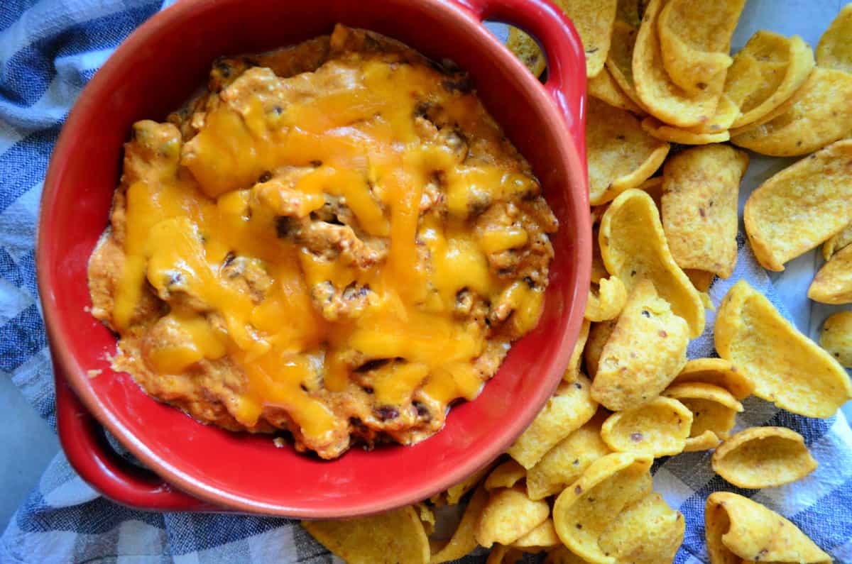 Top view of Chili Cheese Dip in a red bowl served with side of fritos.