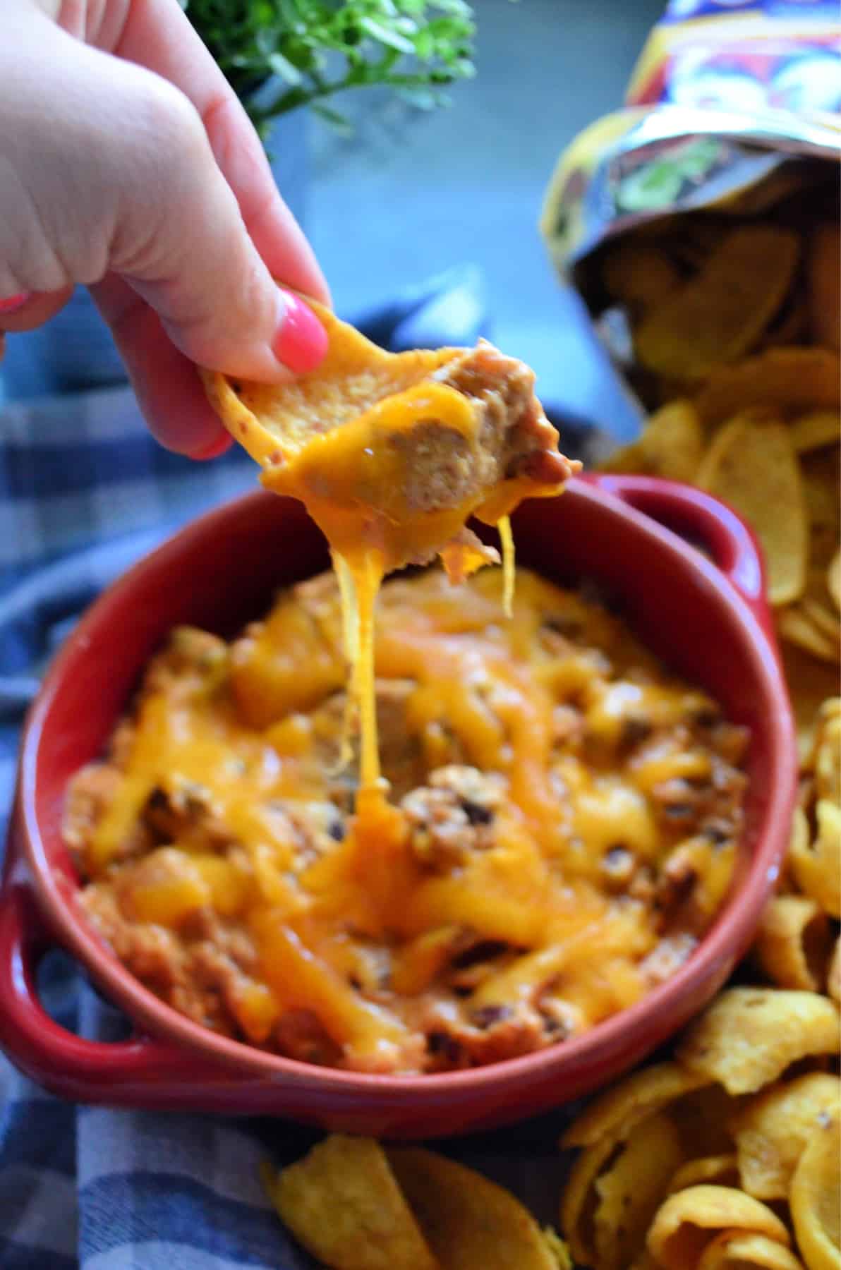 Hand scooping Slow Cooker Chili Cheese Dip with a Frito.