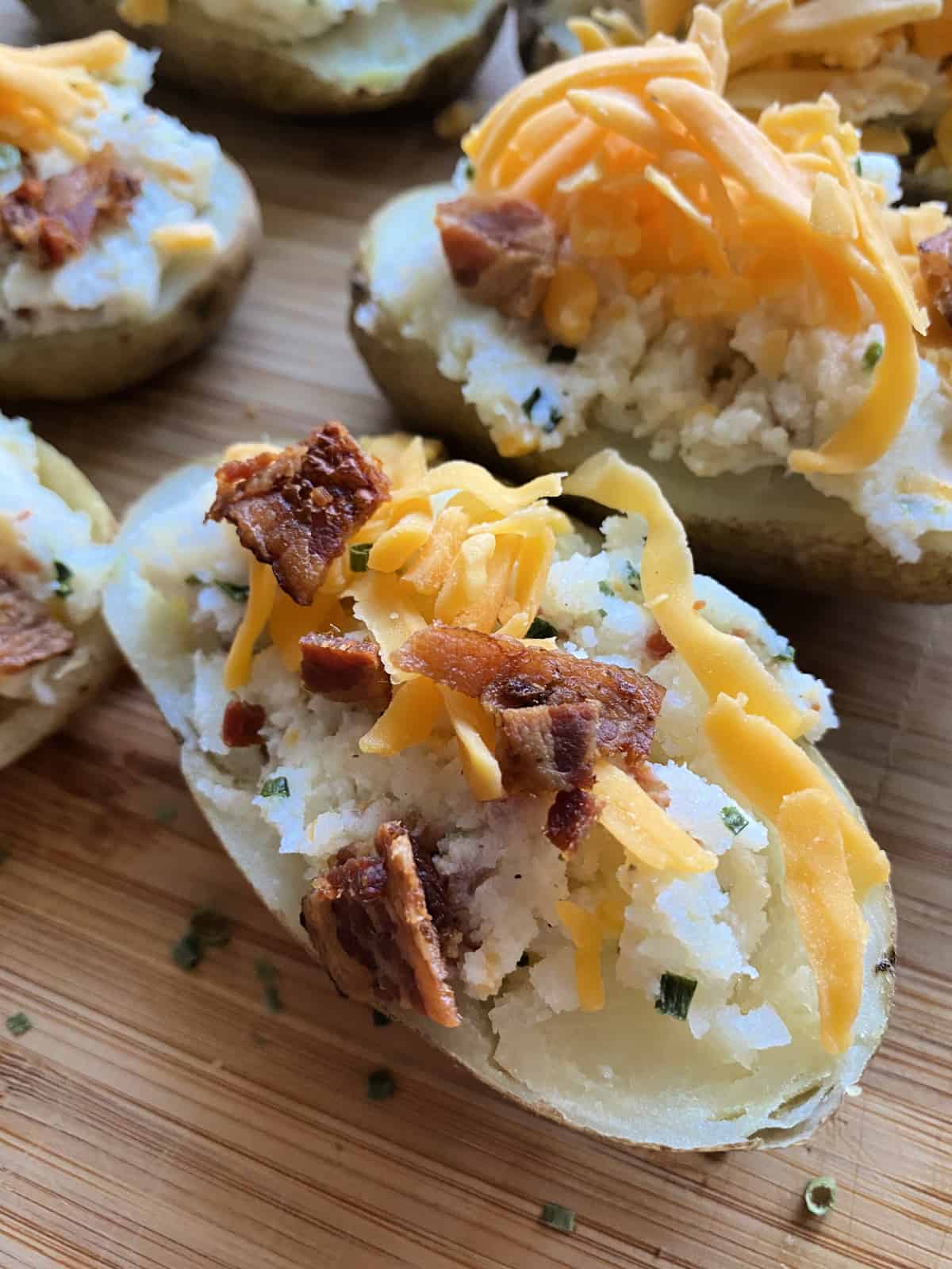 Close up of loaded halved potatoes topped with shredded cheddar and bacon prior to melting.