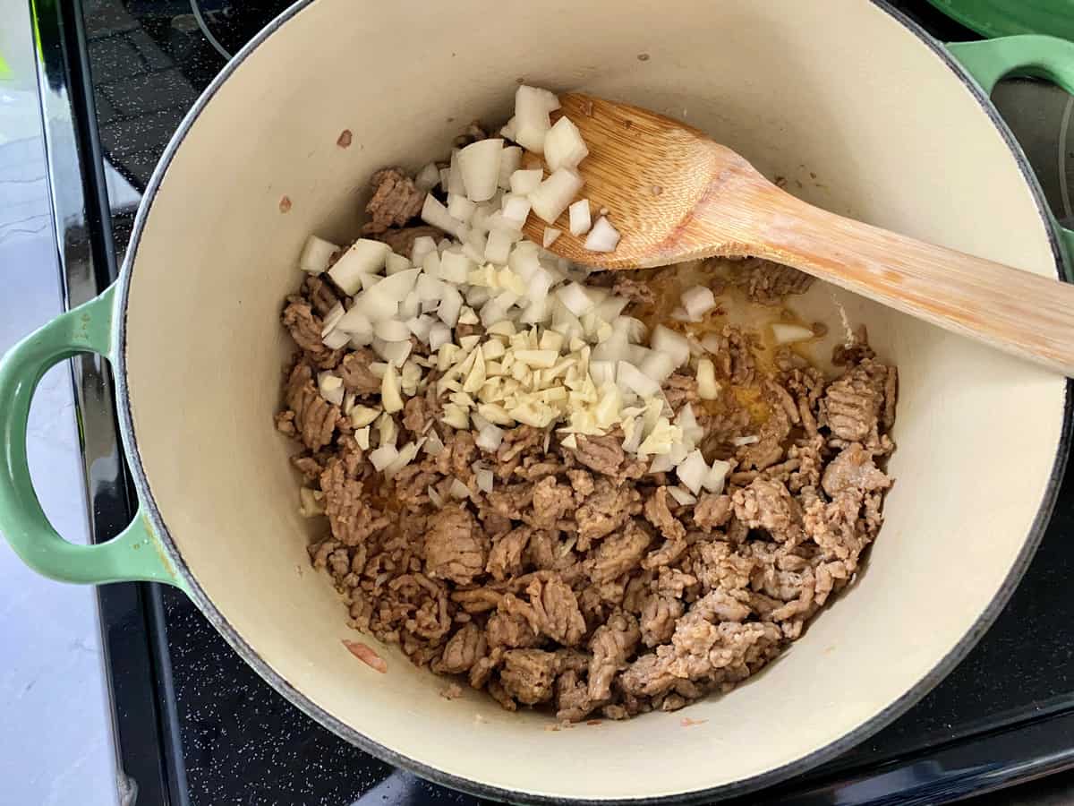 Broken up Italian Sausage, diced onion, minced garlic in a Le Creuset cast iron pot with wooden spoon.