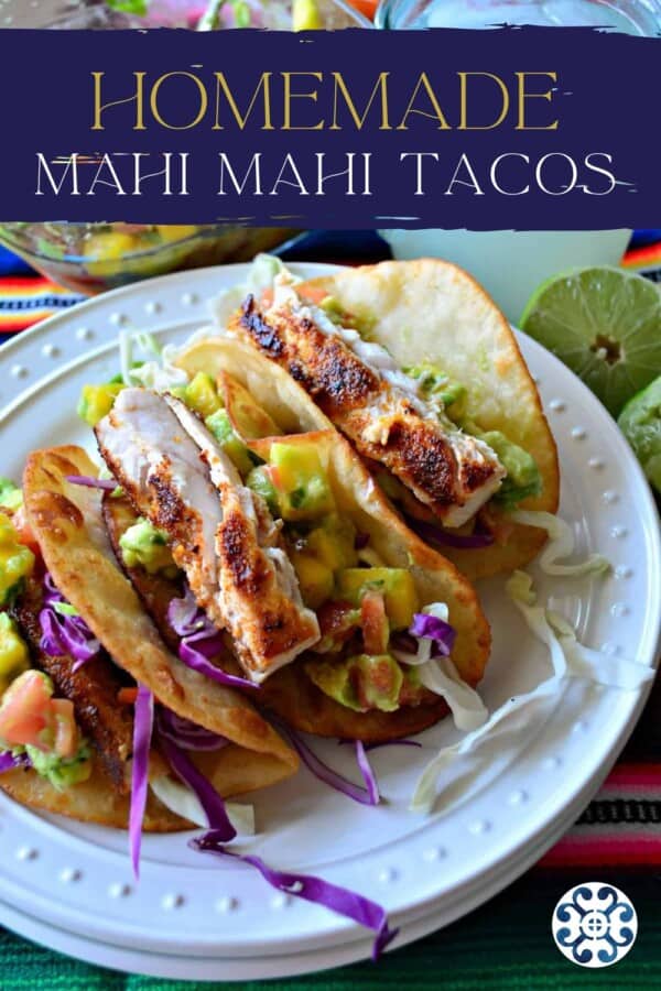 3 tacos with fish, cabbage, avocado, and mango on a white plate with recipe title text on image for Pinterest.