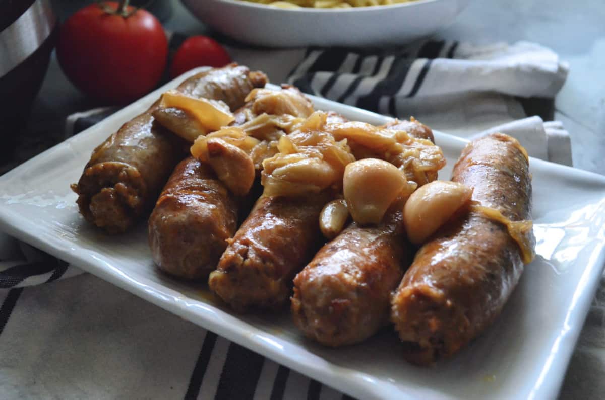 Italian sausage topped with cooked garlic and onions on a platter.