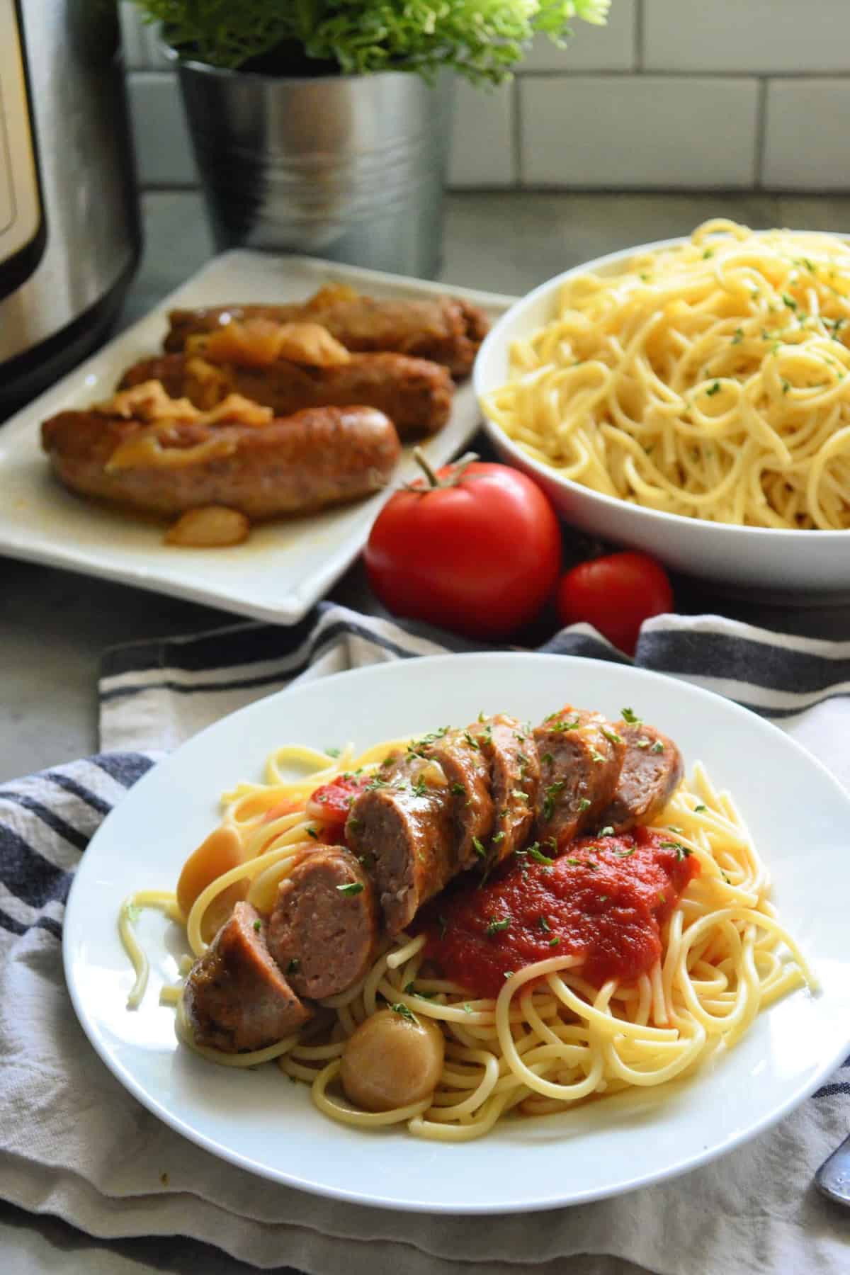 plated spaghetti with marinara and italian sausage in front of spaghetti bowl and sausage platter.