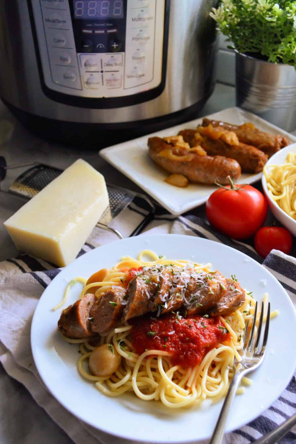 plated spaghetti with marinara and italian sausage in front of spaghetti bowl and sausage platter.