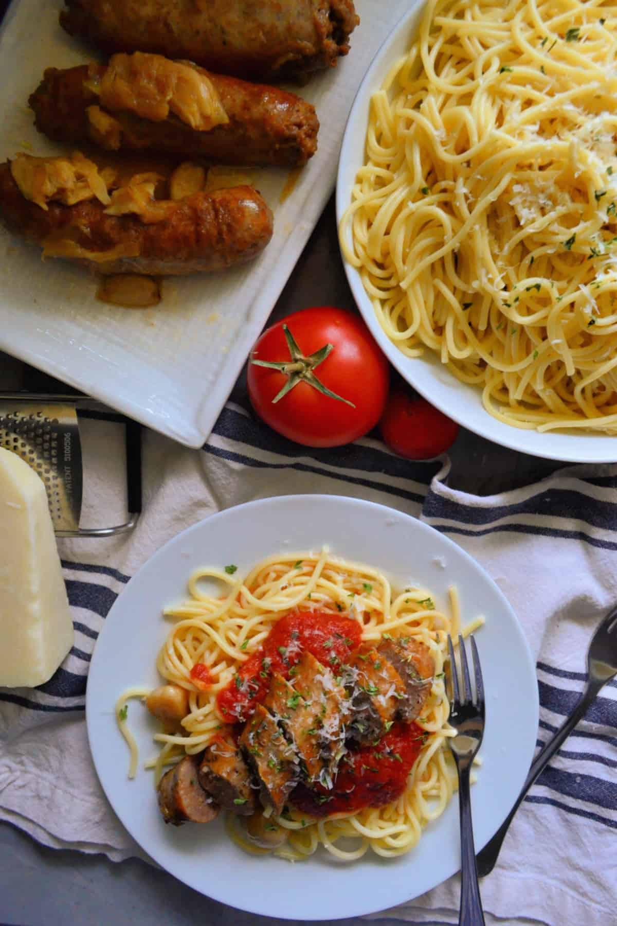 Top view of plated spaghetti with marinara and italian sausage next to spaghetti bowl and sausage platter.