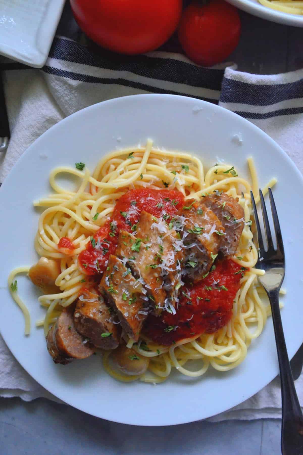 top view close up plated spaghetti with marinara, herbs, sliced italian sausage and a fork.