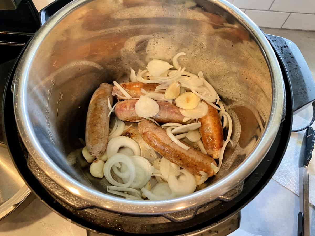  widok z góry na pół ugotowaną włoską kiełbasę w garnku z surową cebulą i czosnkiem. 