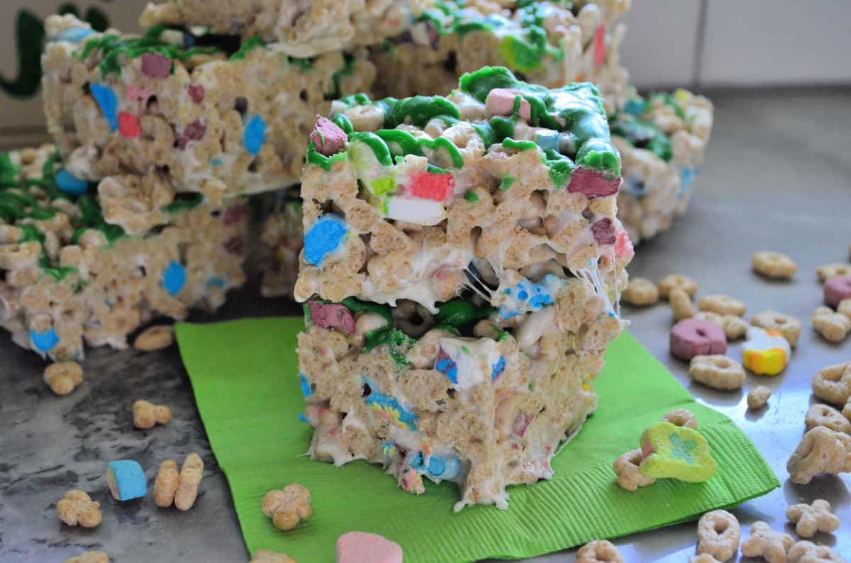 lucky charms cereal treats cut into cubes, drizzled with green chocolate, and stacked on napkin.