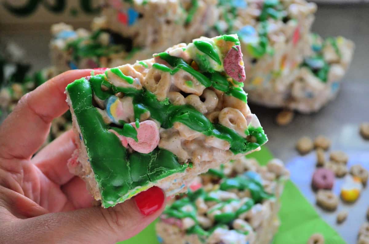 Hand holding lucky charms treat drizzled with green chocolate up close.