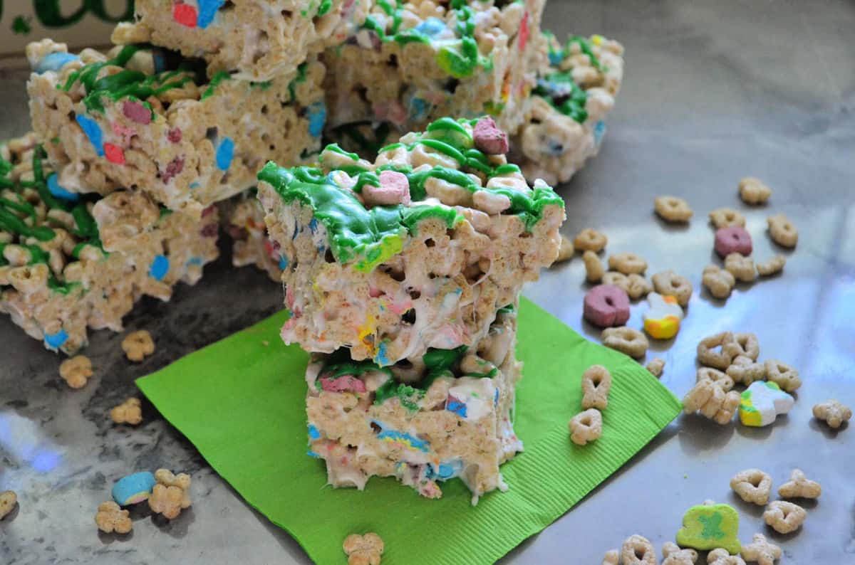 lucky charms cereal treats cut into cubes, drizzled with green chocolate, and stacked on napkin.