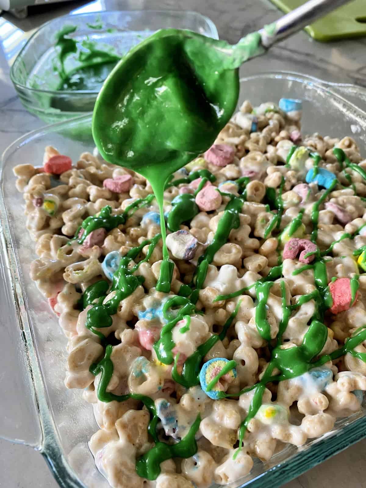 Drizzling green dyed white chocolate on top of Lucky Charms Cereal Treats in casserole dish.