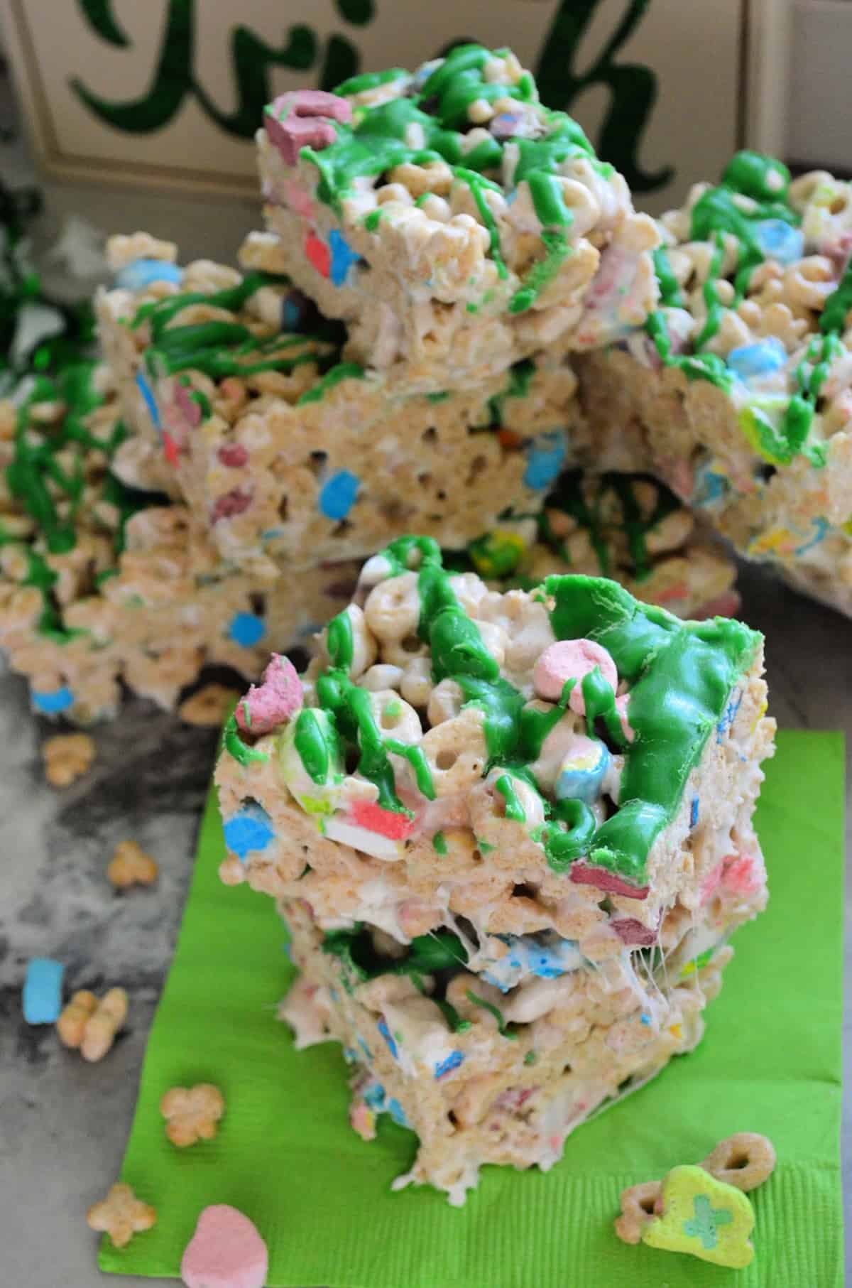 closeup of lucky charms cereal treats cut into cubes, drizzled with green chocolate, and stacked.