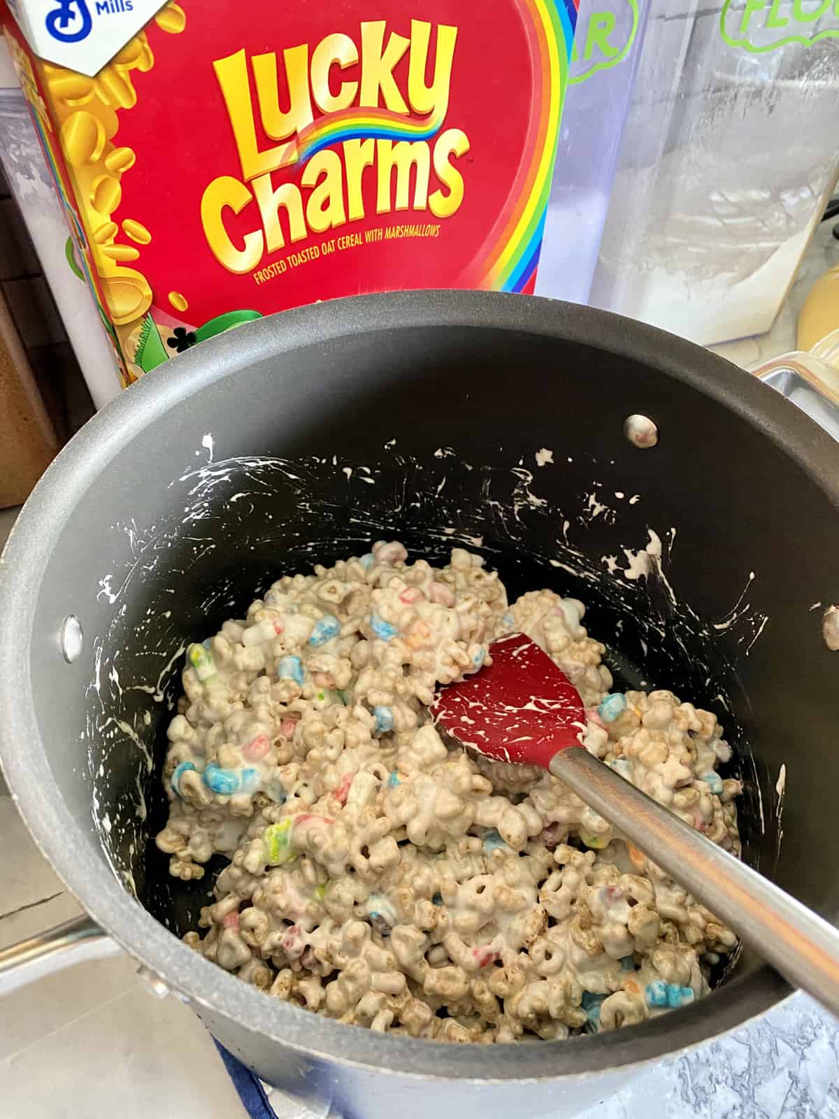 Melted marshmallows, butter, and lucky charms cereal in large stock pot being stirred with spatula.