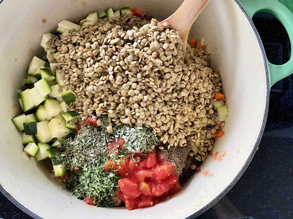 Ingredients (lentils, tomatoes, zucchinis, herbs, carrots, celery, onion, garlic, and ground pork) in large dutch oven.