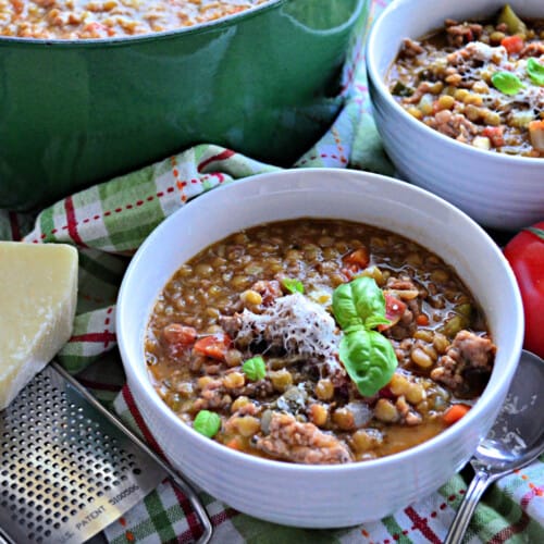 Two white bowls with lentil soup with a green pot in the background.