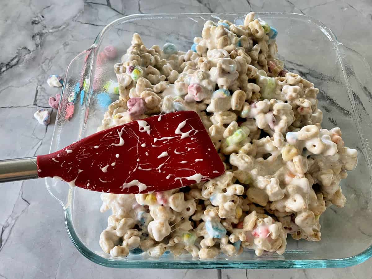 lucky charms cereal mixed with melted butter and marshmallows in glass casserole dish.