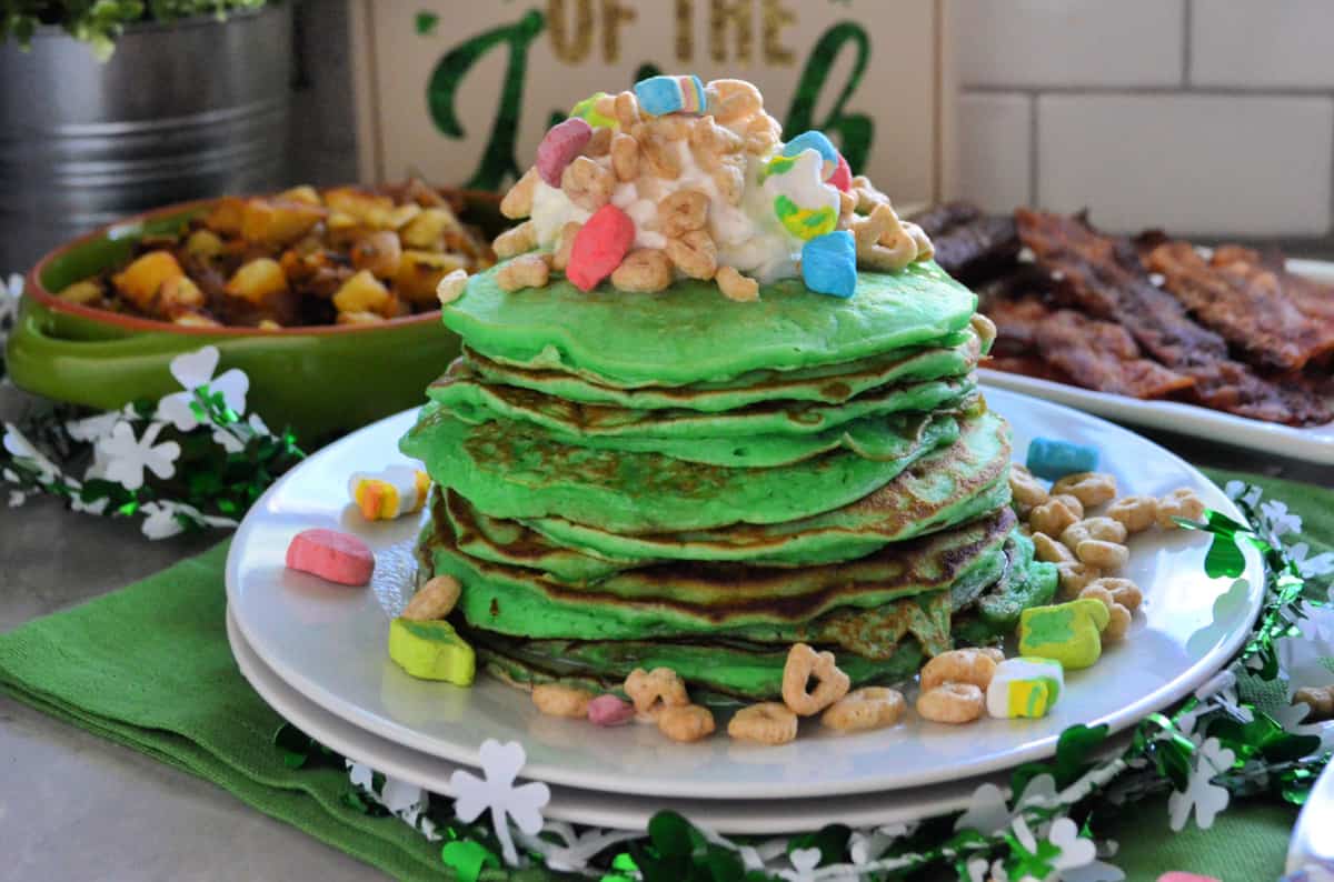 side view of plated stacked green pancakes topped with melted marshmallow and lucky charms.