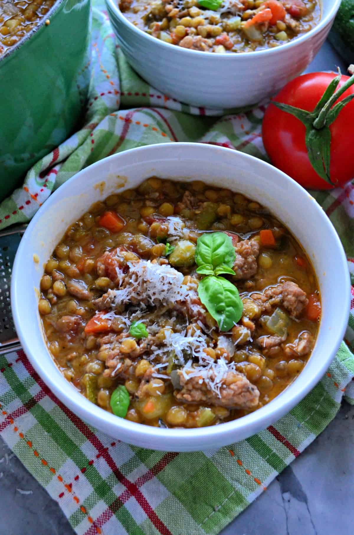 close up top view of Sausage Lentil Soup in white bowl topped with parmesan and sprig of basil.