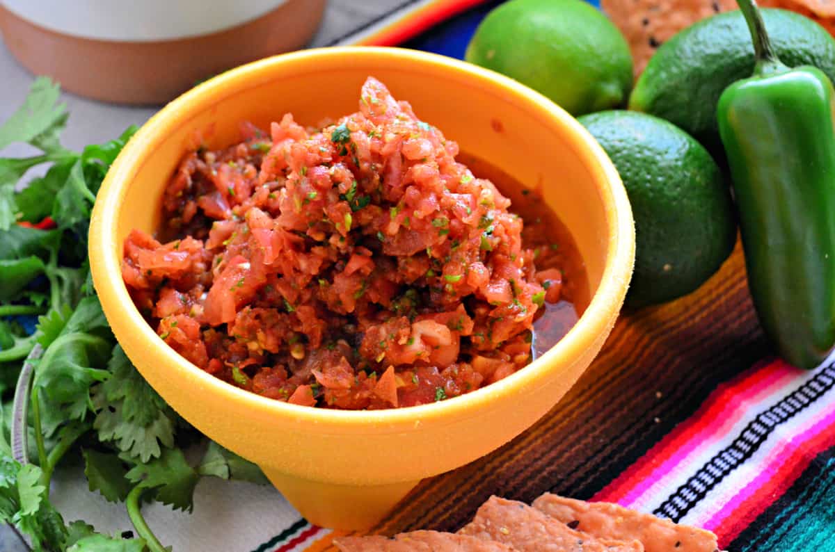 Yellow bowl with tomato salsa with limes, jalapeno, and cilantro next to it.