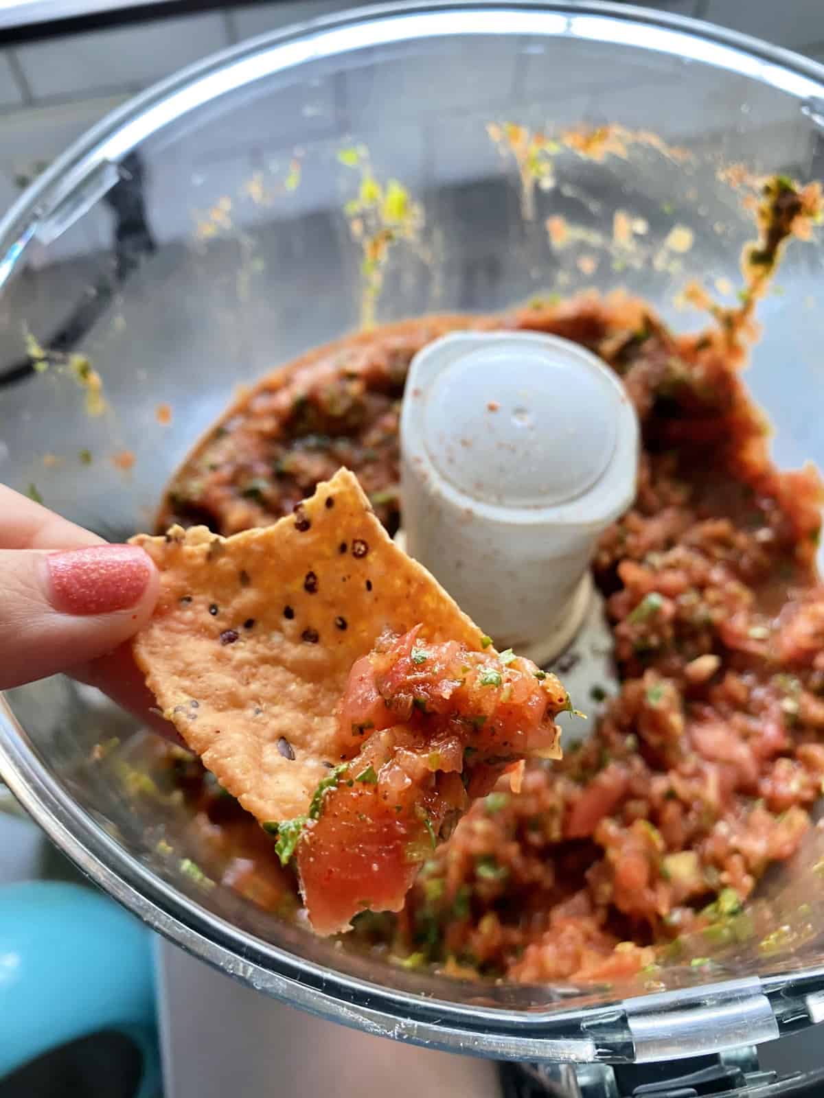 Female hand holding a chip dipping into a food processor with salsa.