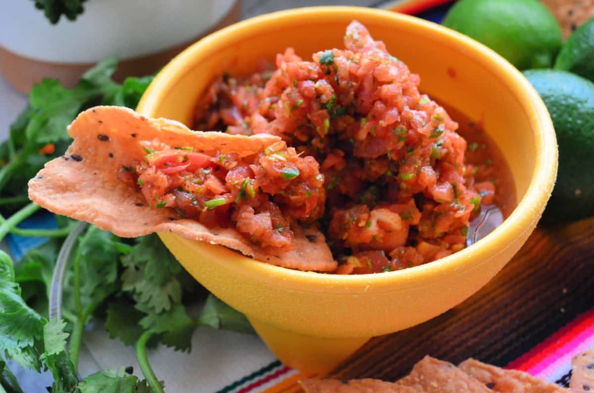 Yellow bowl filled with salsa and a chip scooped with salsa.