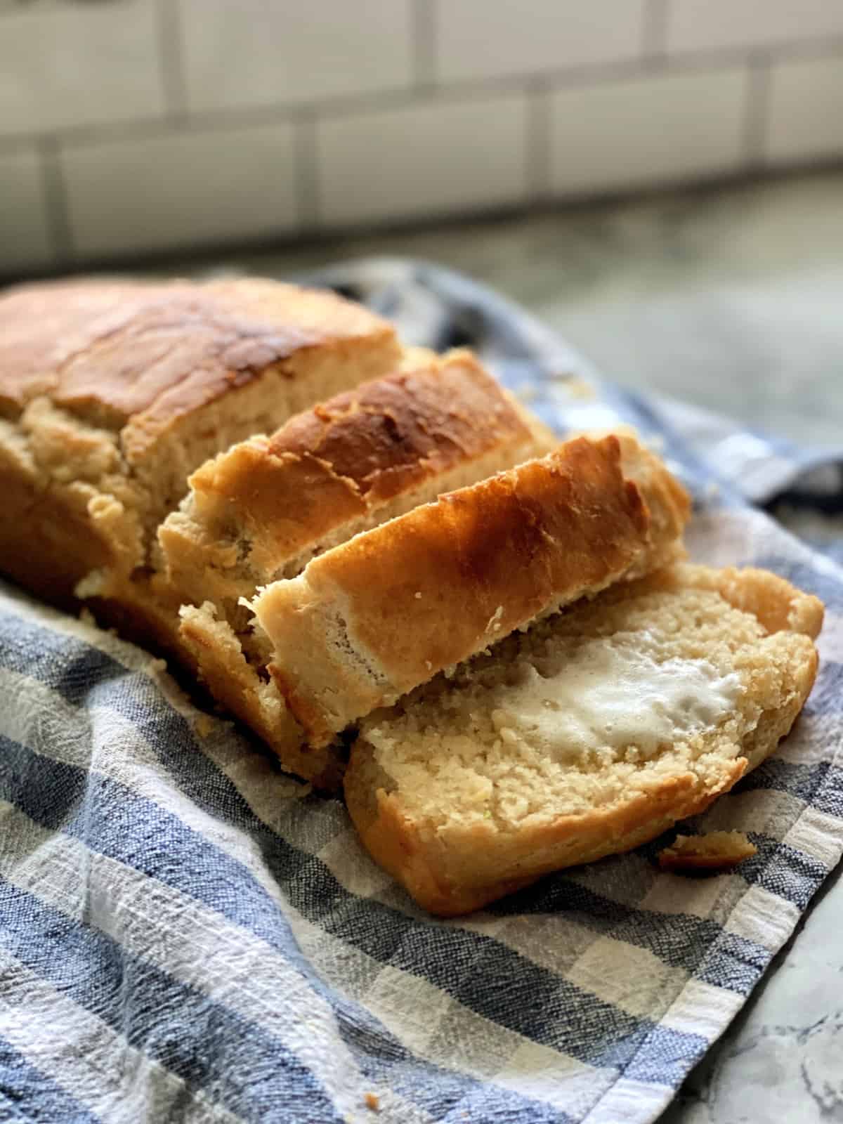 Sliced loaf of golden brown beer bread on a tablecloth with butter melting on one slice.