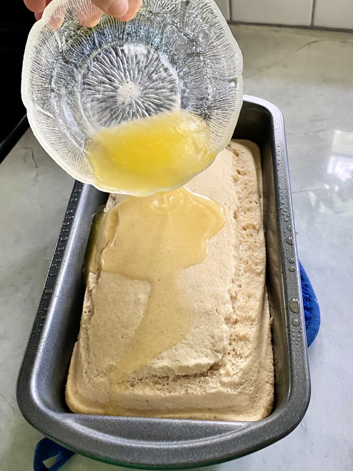 Pouring melted Butter on half baked Bread in bread pan.