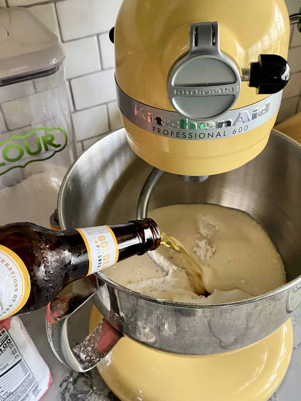 Pouring beer into beer bread batter in a yellow KitchenAid Professional 600 mixing bowl.