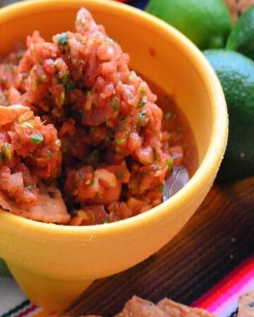 Close up of corn chip dipped in red salsa in small bowl.