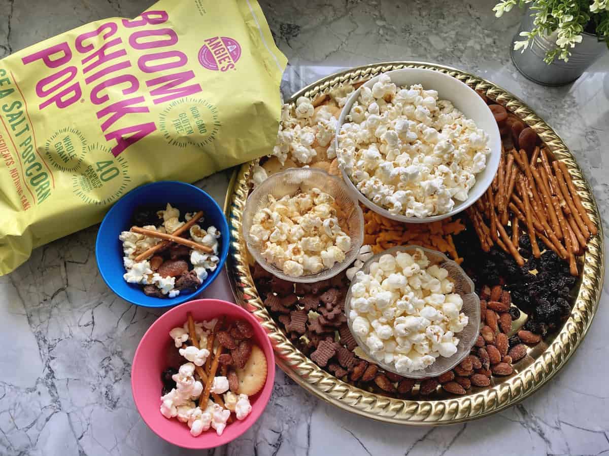 platter with crackers, pretzels, dried fruits, 3 popcorn flavors next to two small bowls of snack.