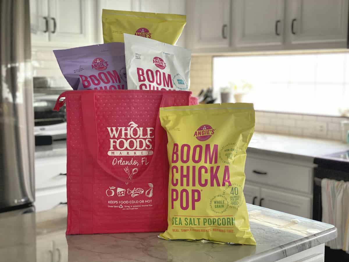 Angie’s BOOMCHICKAPOP® Sea Salt Popcorn next to Whole Foods bag containing 3 other flavors.