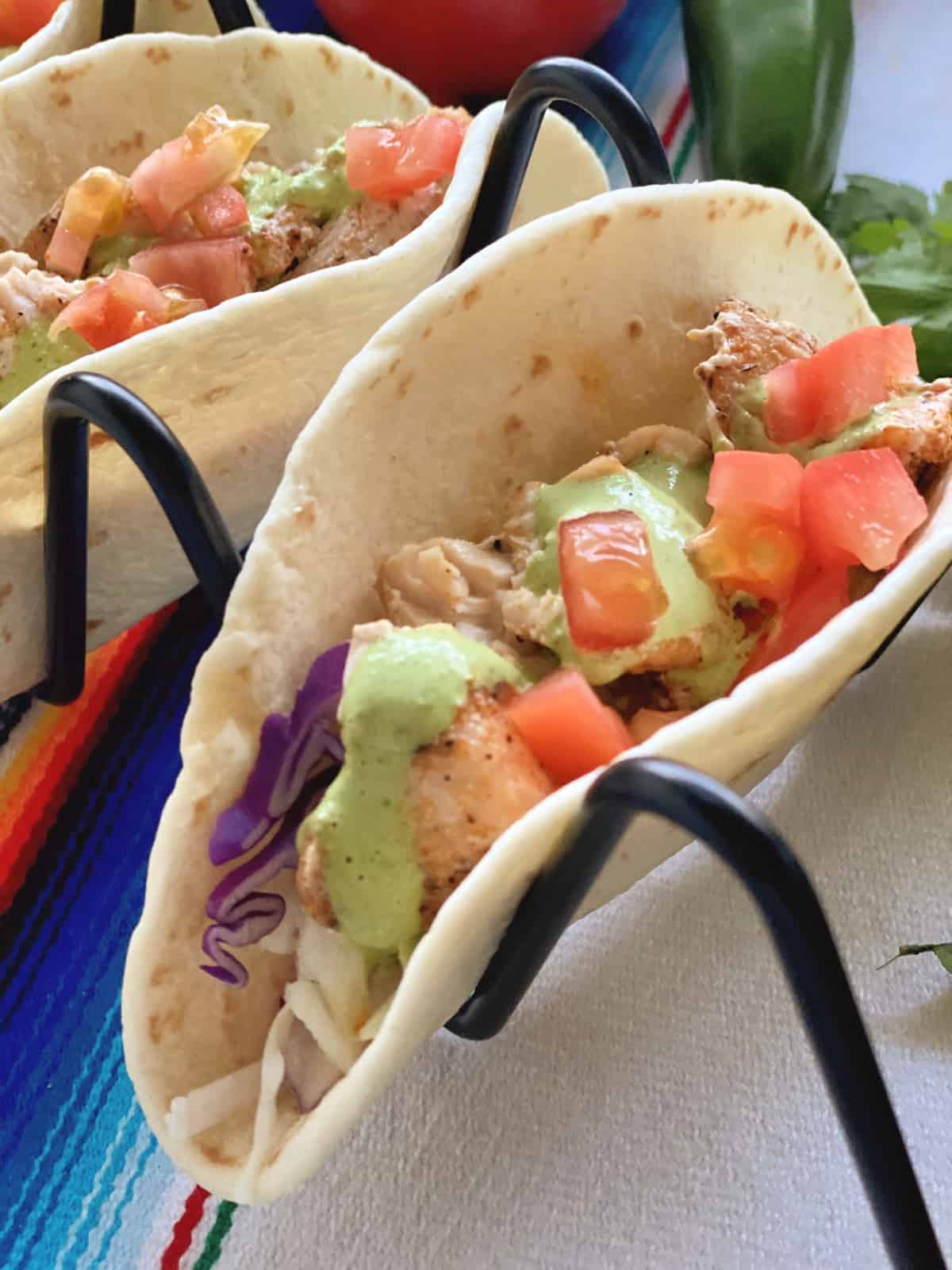 closeup of two fish tacos topped with tomatoes and cilantro dressing in wire holders.