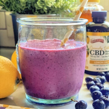 Blueberry Lemon Smoothie in a glass surrounded paper straws, fresh lemon, and blueberries.