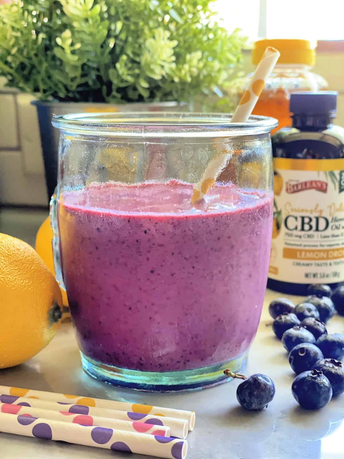 glass containing a purple blended liquid with a paper straw and Barlean's CBD oil in background.