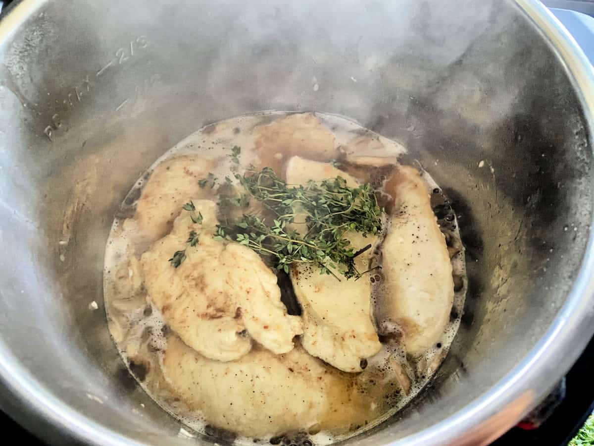 Top view of browned chicken cutlets in the Instant Pot toped with sprigs of fresh thyme.