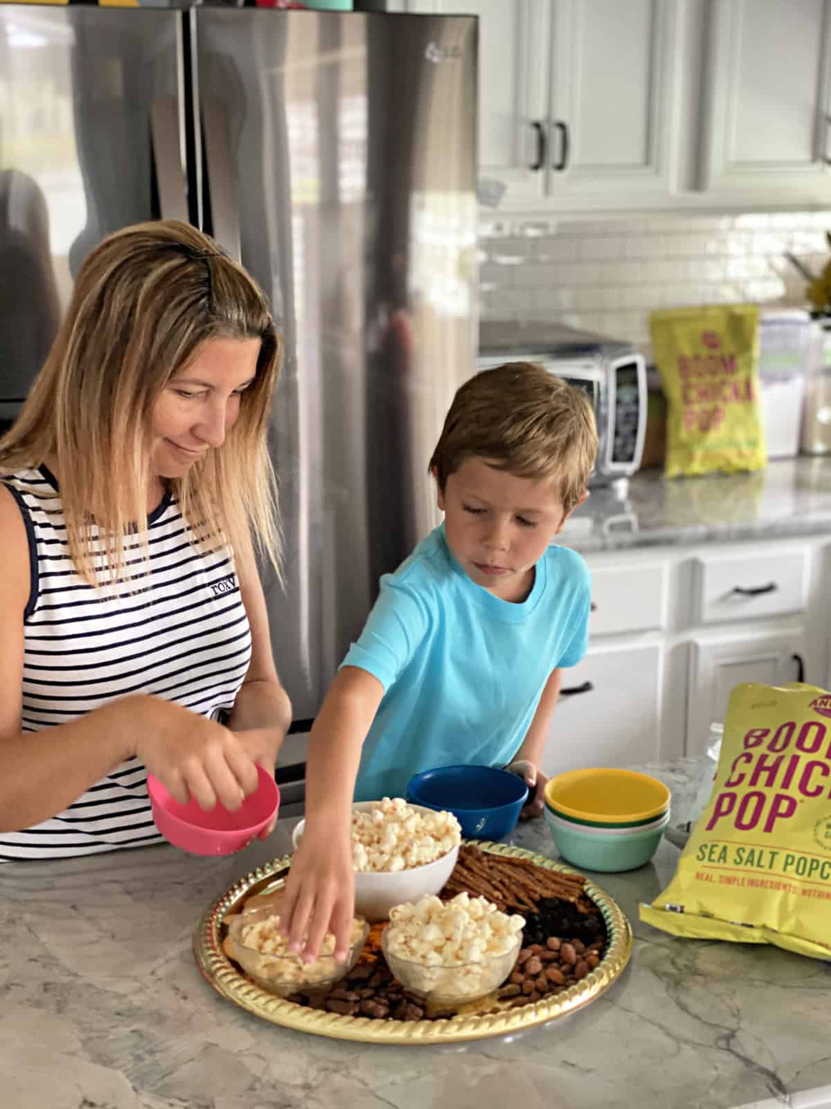 Mother and son putting together snack plater at kitchen countertop with fridge in background.