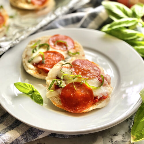 Cooked English Muffin Pepperoni Pizzas on white plate garnished with basil.
