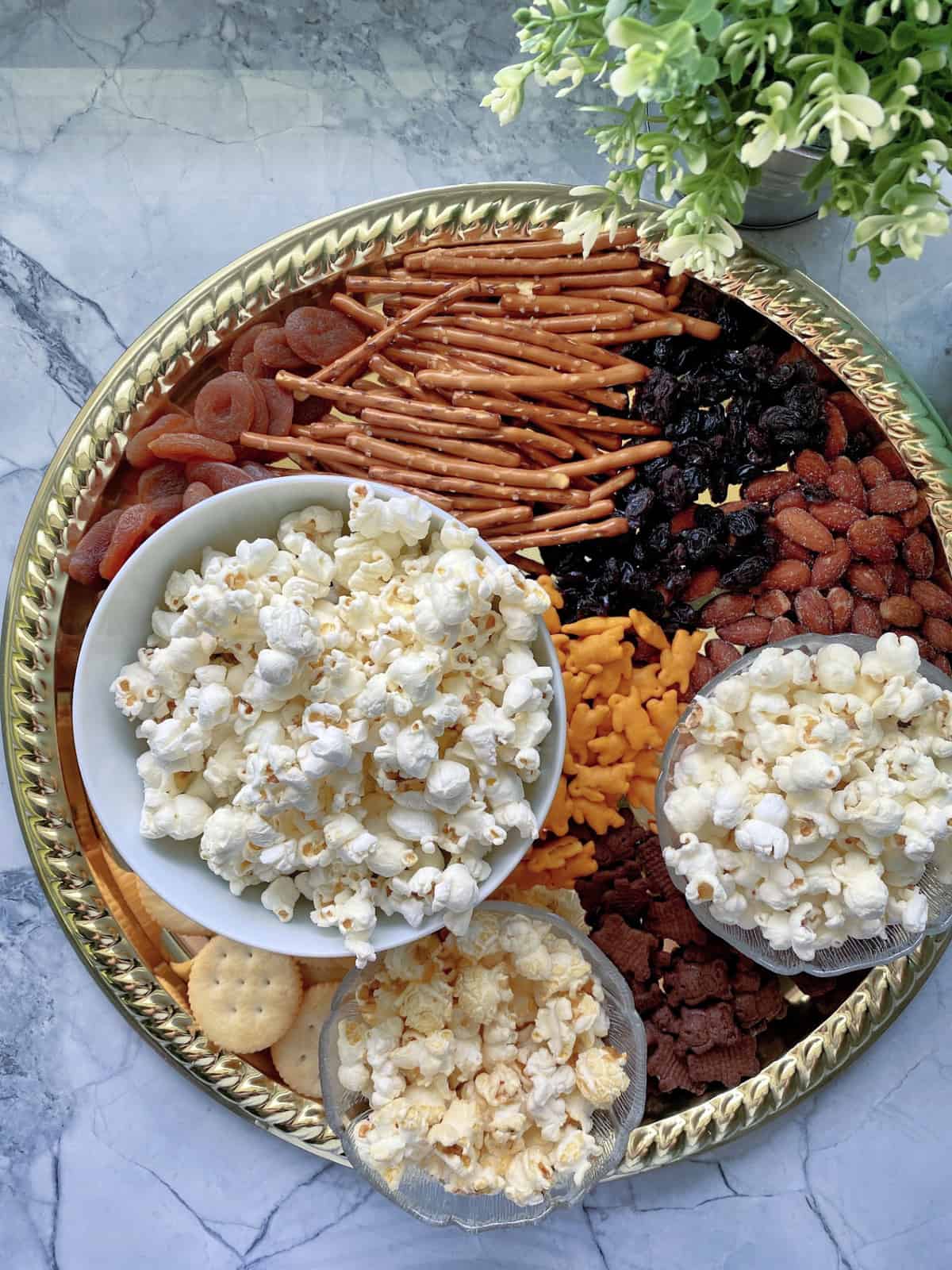 top view platter with 3 popcorn bowls, dried fruits, pretzels, crackers, and cheddar bunnies.