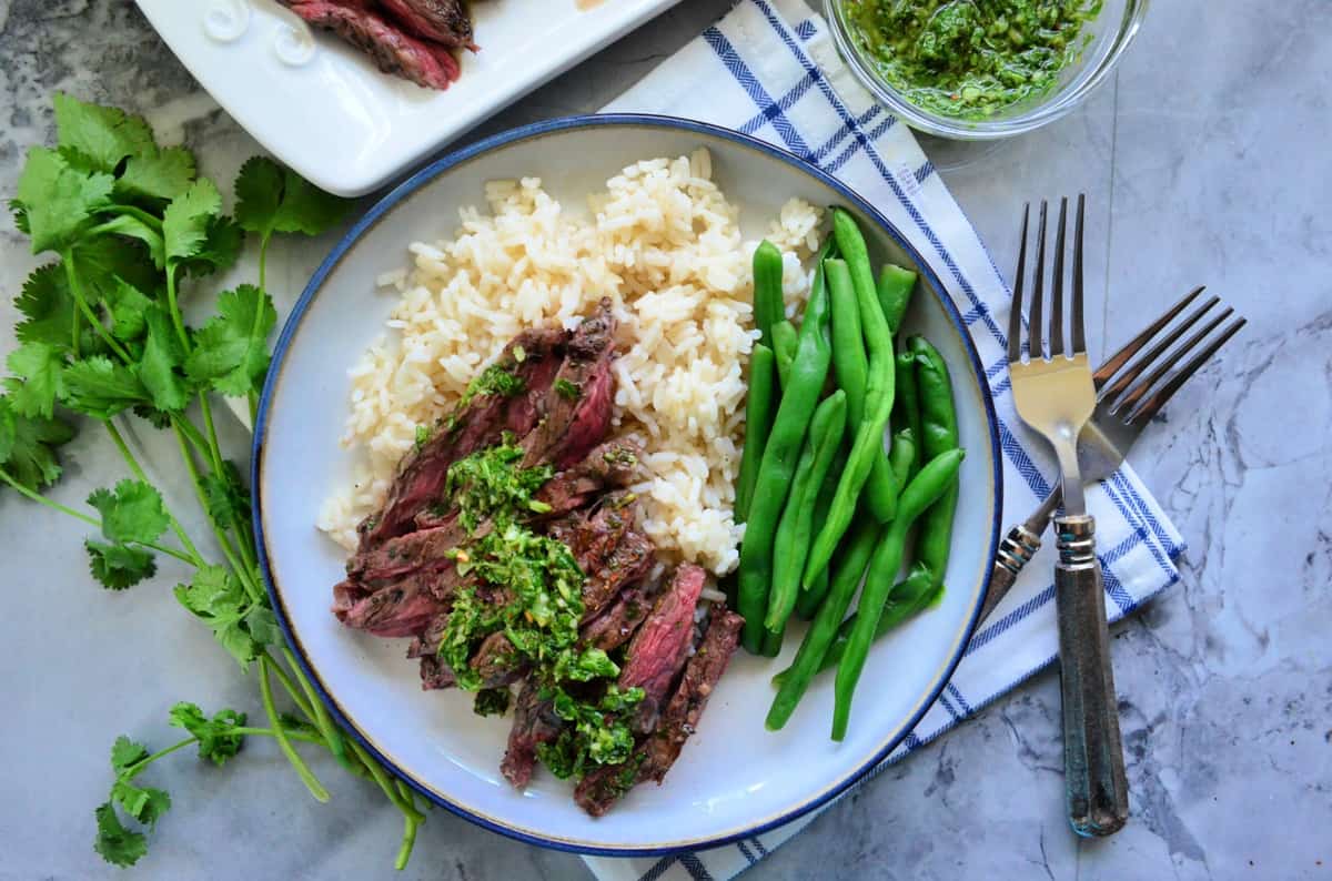 top view of plated Grilled Skirt Steak with Chimichurri Sauce with green beans over rice bed.