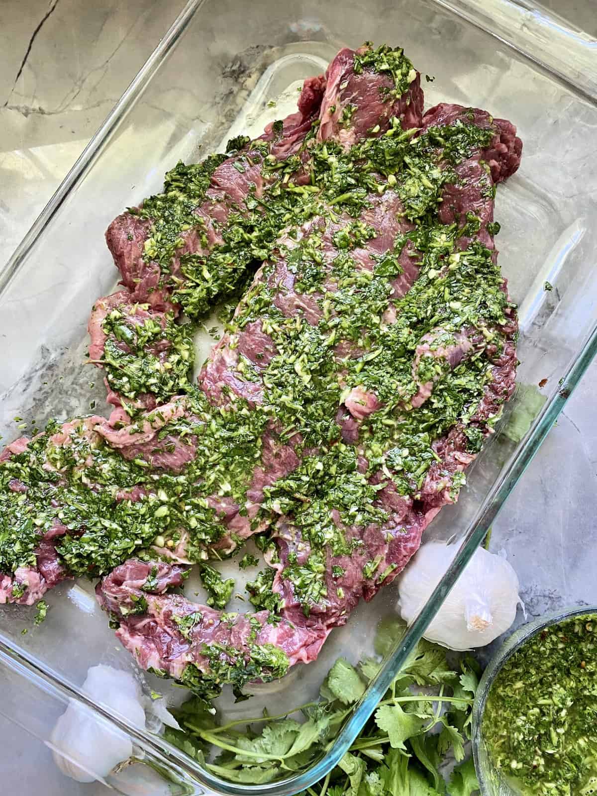 top view Grilled Skirt Steak in a glass dish marinading in Chimichurri Sauce.