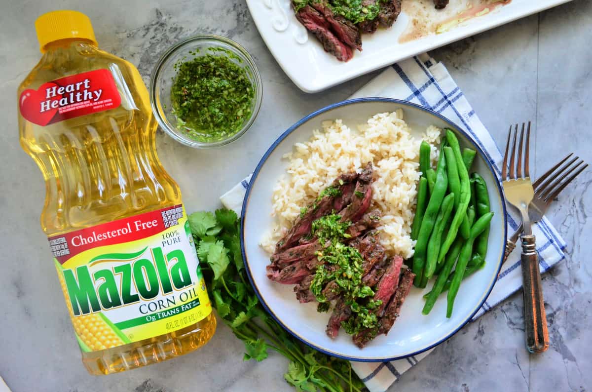 plated Skirt Steak with Chimichurri Sauce with green beans over rice bed near mazola corn oil bottle.