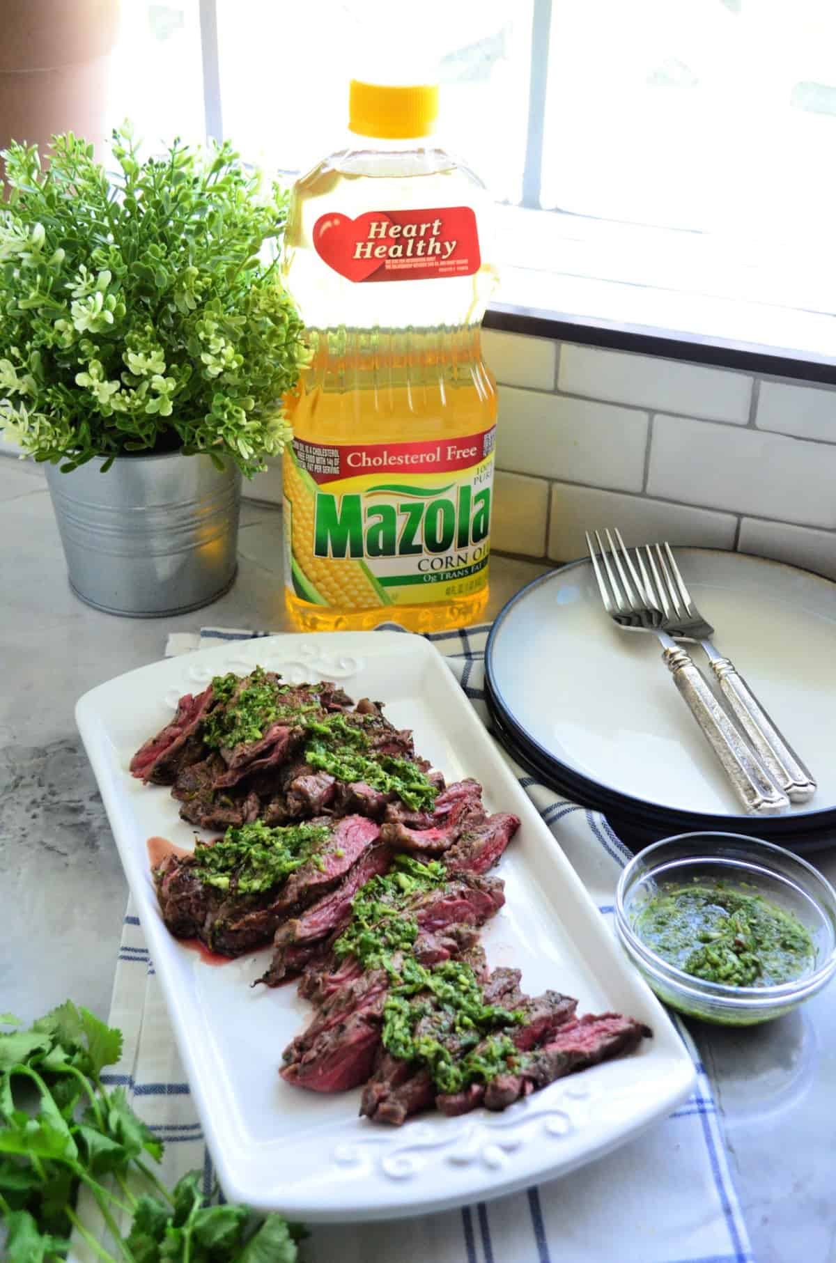 platter of sliced Grilled Skirt Steak topped with Chimichurri Sauce in front of Mazola Corn Oil.